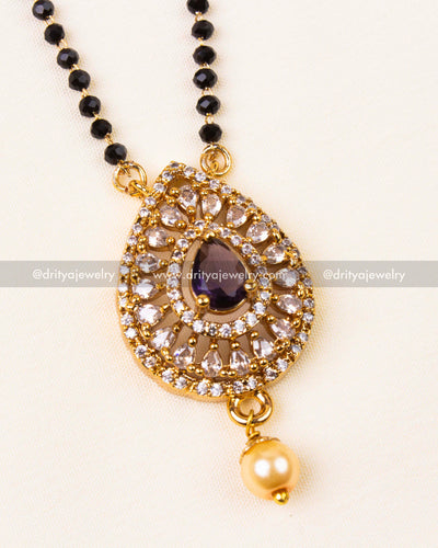 Purple gemstone pendant set in gold with shimmering accents and pearl drop.