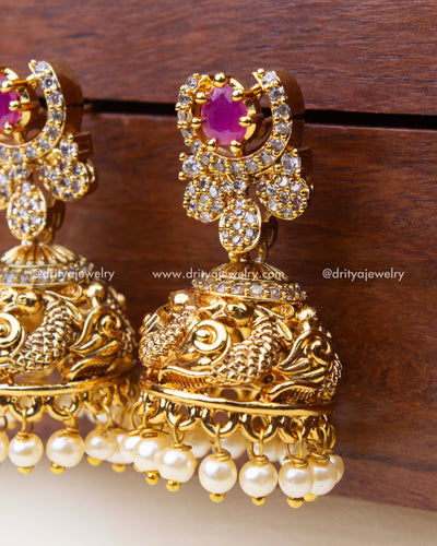 Detailed view of pink stone Antique jhumkas featuring peacock carving and pearl danglers.