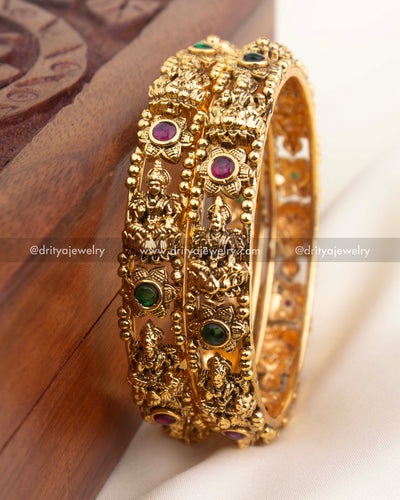 Detailed close-up of temple bangles with goddess engravings, beaded borders, and multicolor stone accents in antique finish.
