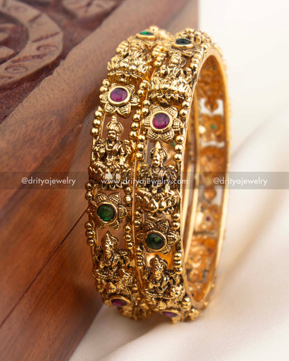 Detailed close-up of temple bangles with goddess engravings, beaded borders, and multicolor stone accents in antique finish.