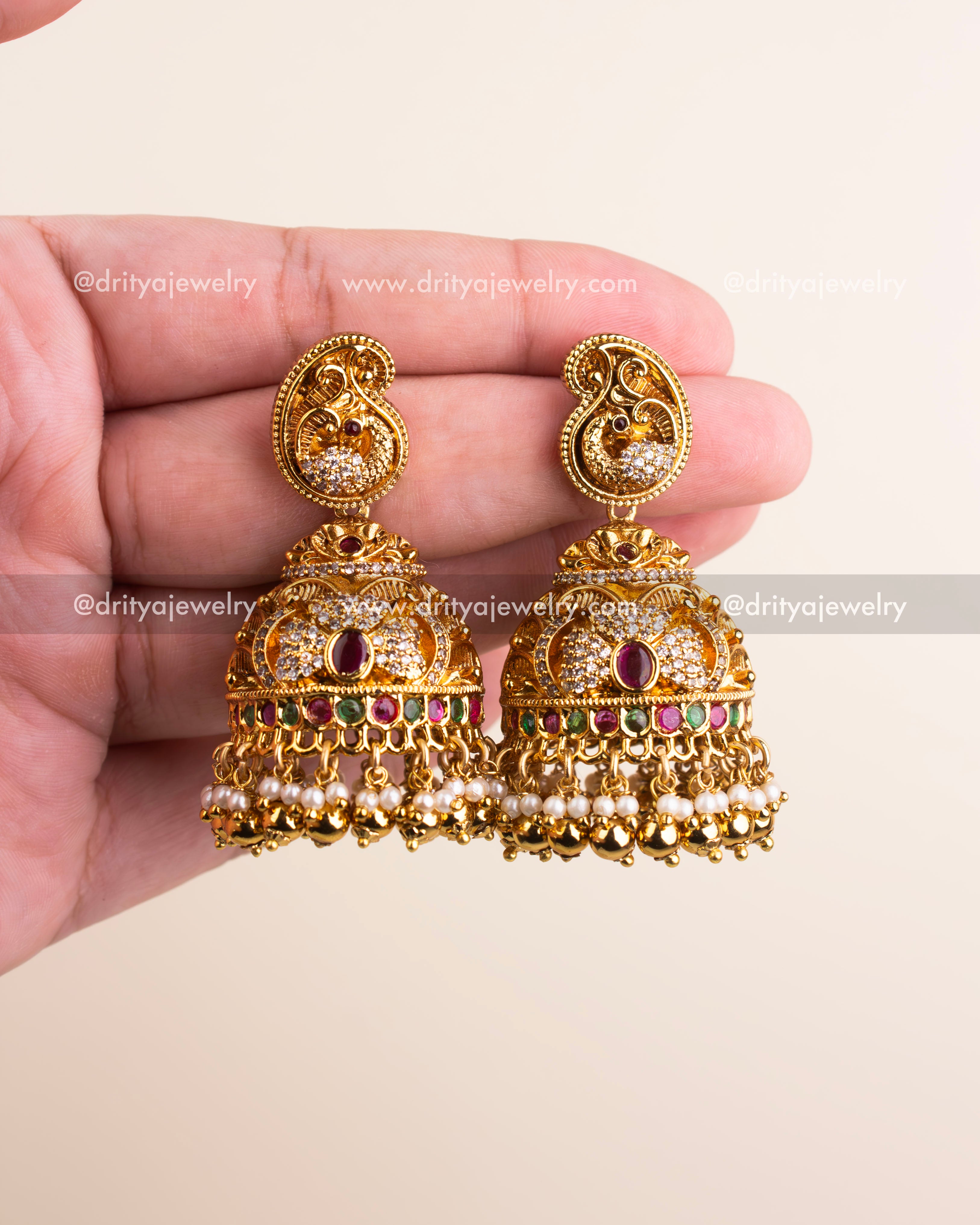 Detailed view of dome-shaped jhumka earrings featuring ruby and green stones with layered pearl and gold bead hangings.