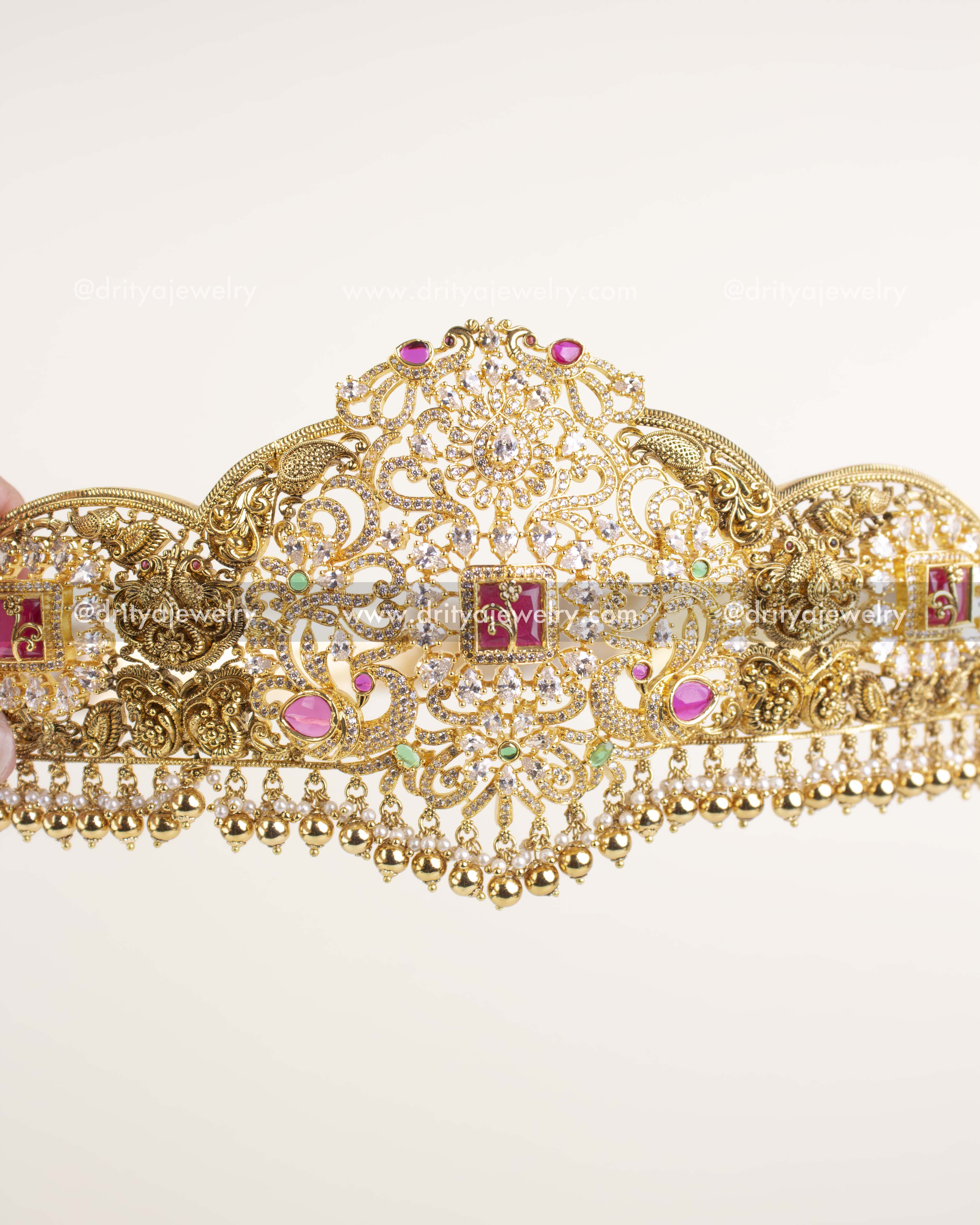 Gold-plated bridal waist belt featuring nakshi detailing, CZ stones, and ruby-green accents.