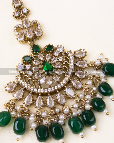 Detailed maang tikka design with emerald green beads and gold antique finish.