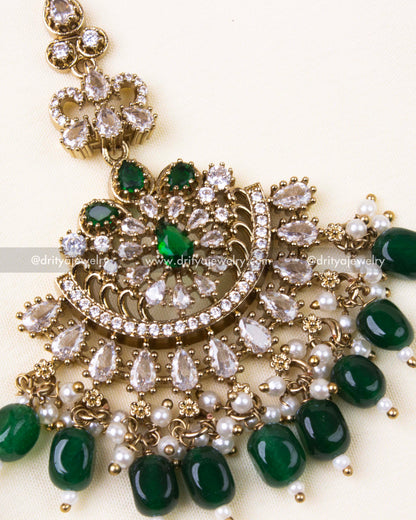 Detailed maang tikka design with emerald green beads and gold antique finish.