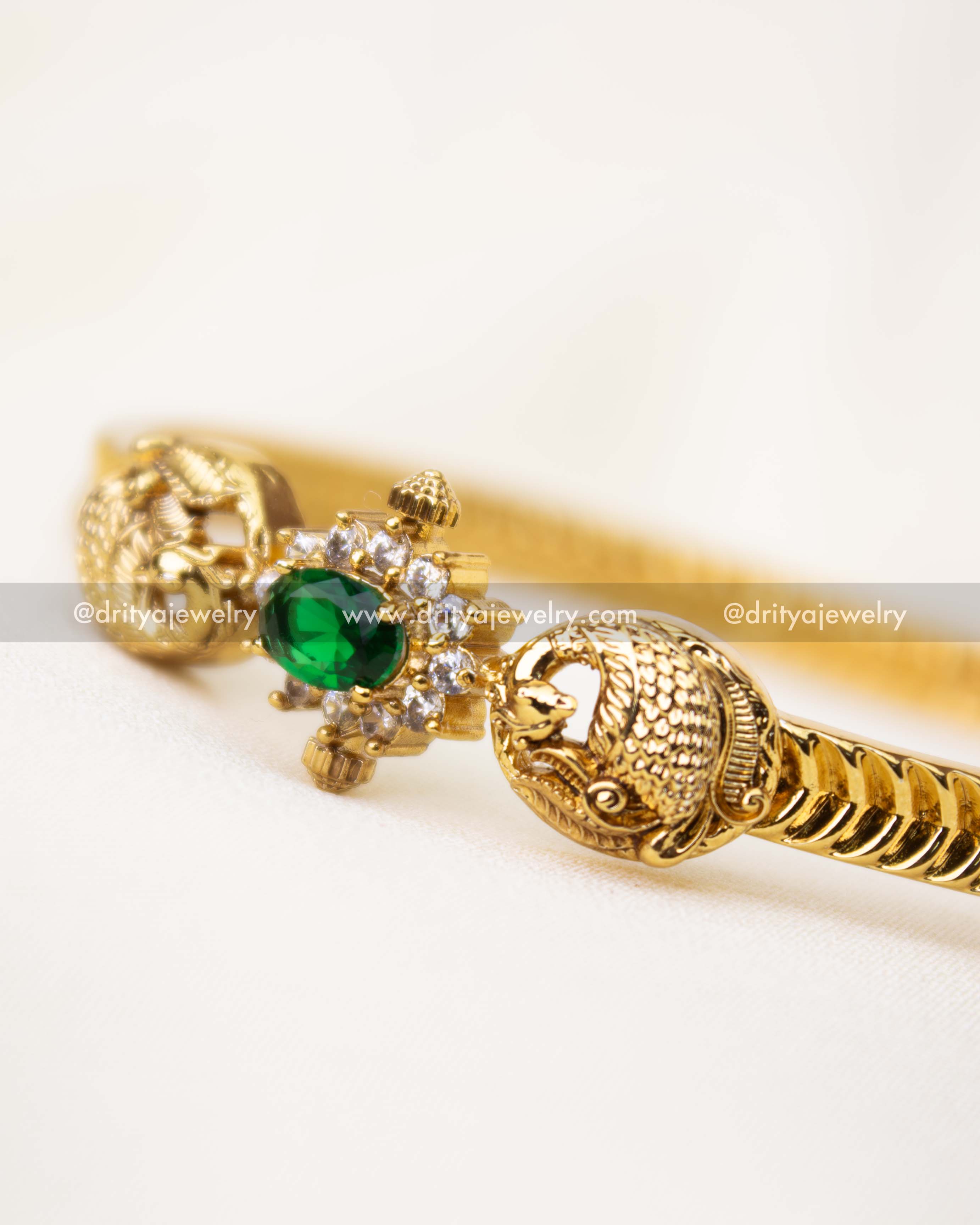 Detailed view of emerald CZ centerpiece with antique gold peacock carvings.