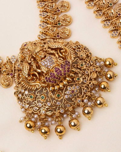 Detailed view of a temple-inspired Lakshmi Devi pendant with antique gold plating, pearl embellishments, and red stones.