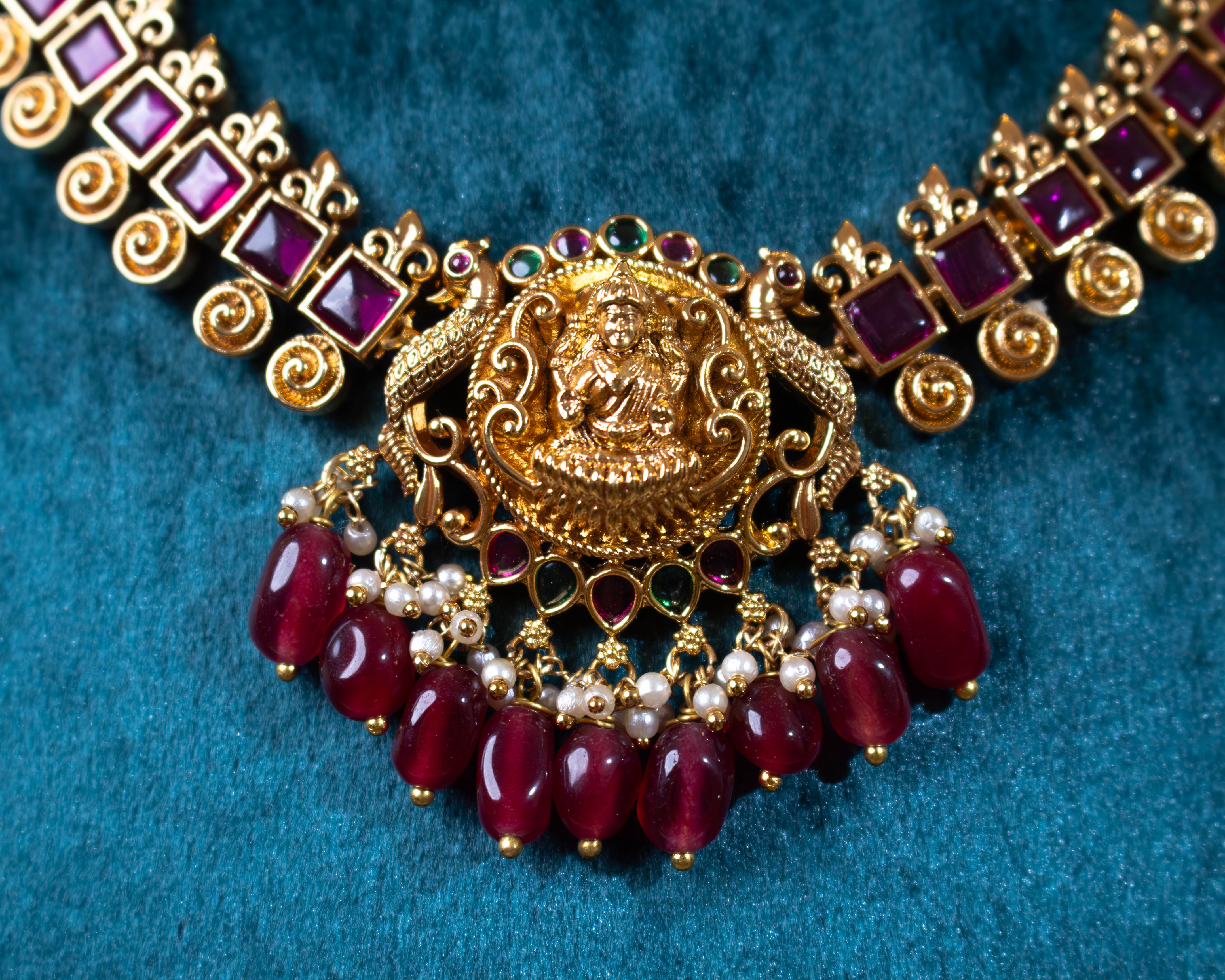 Close-up of the detailed Lakshmi pendant from Dritya Jewelry’s temple necklace set, showcasing ruby beads, pearls, and emerald stone accents in a gold-plated finish.