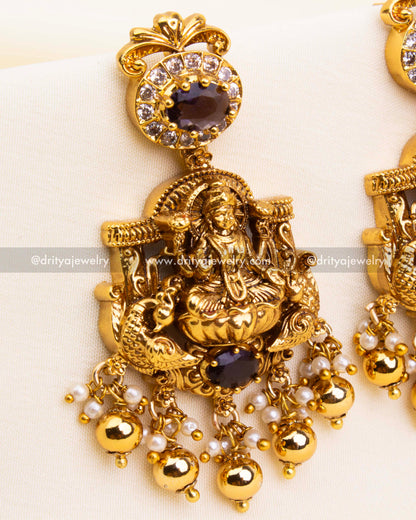 Zoomed-in view of traditional earrings with goddess Lakshmi detailing, purple stone setting, and white CZ embellishments