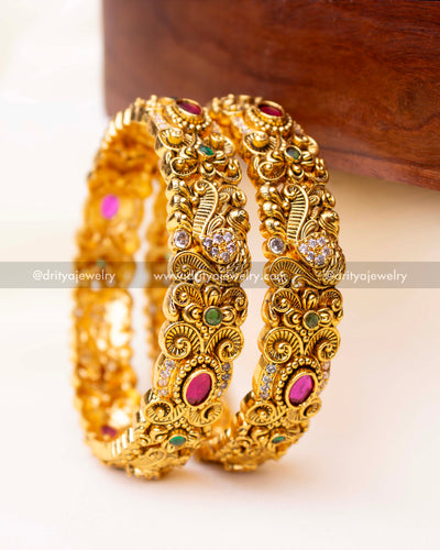 Pair of antique gold-finished Nakshi bangles adorned with ruby-red and emerald-green stones.