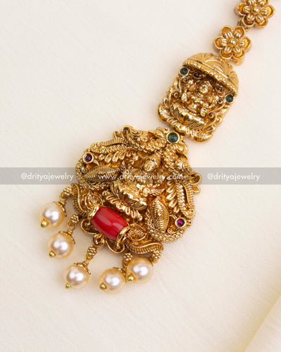 Detailed close-up of premium nakshi maang tikka with intricate carvings, coral bead, and pearls.