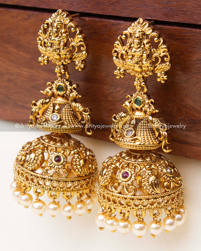 Detailed view of grand temple Jhumka earrings showing peacock and floral carvings with pearls.