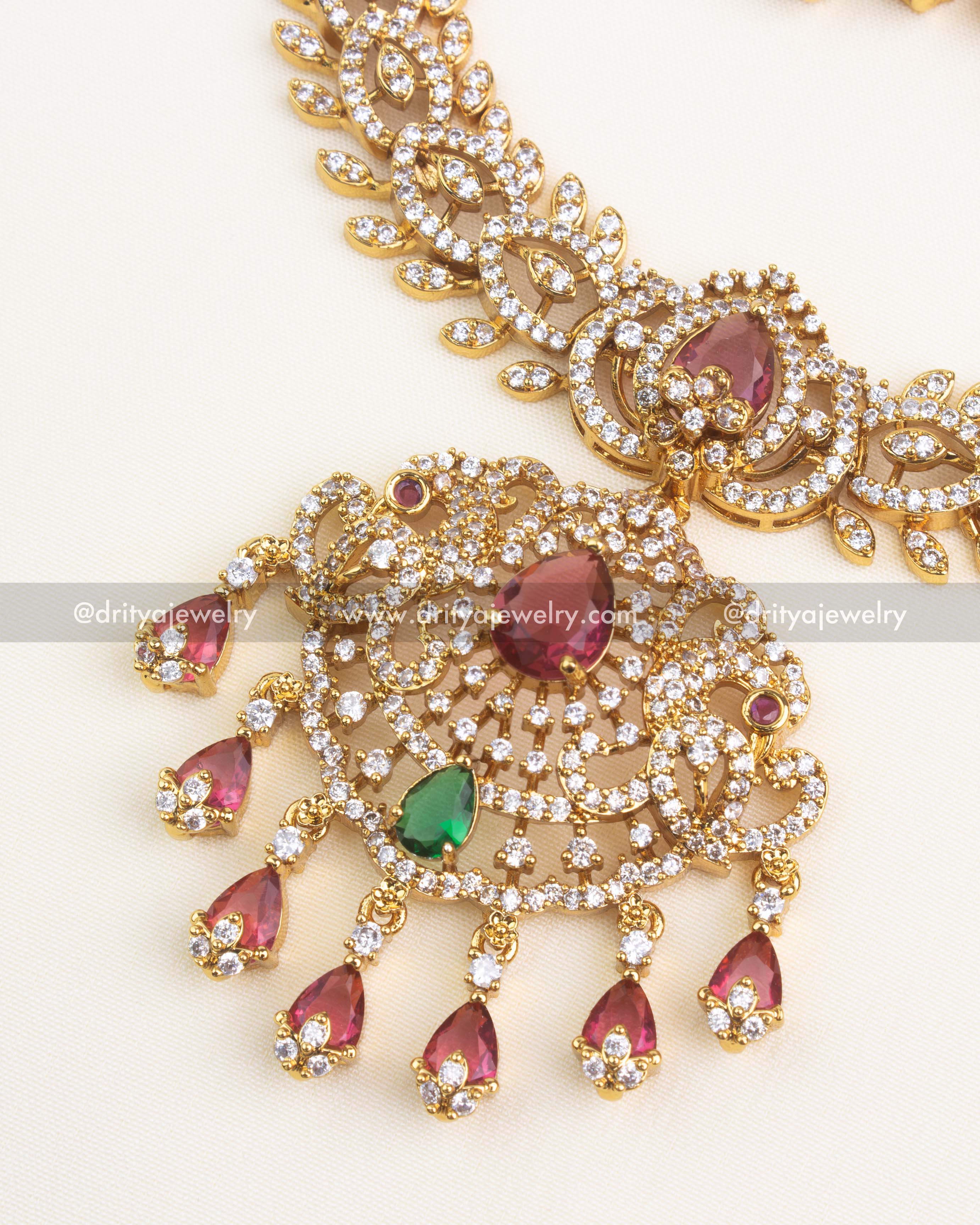 Intricate circular pendant with ruby teardrop centerpiece, emerald accent, and CZ border.