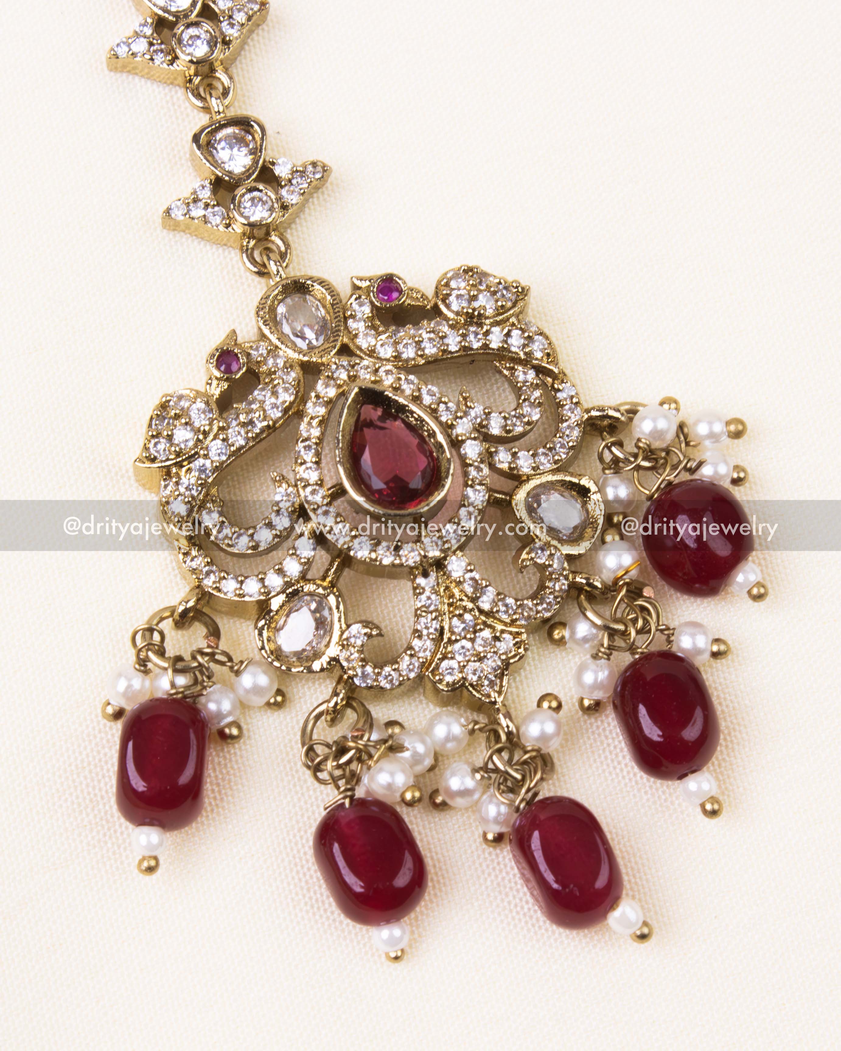 Zoomed view of gold-toned tikka with red stones and vintage design.