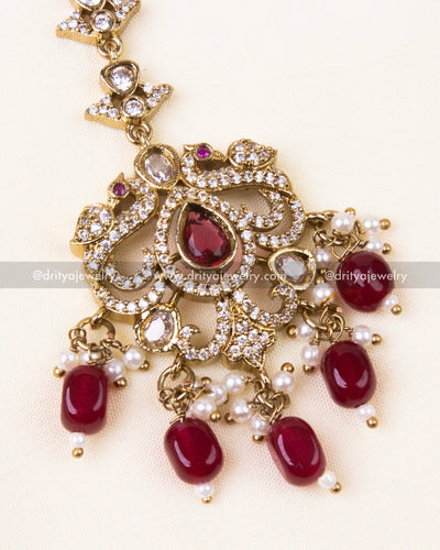 Zoomed view of gold-toned tikka with red stones and vintage design.