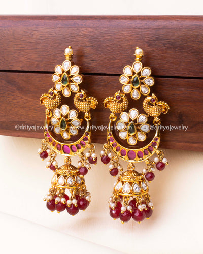 Close-up view of dual peacock earrings with Kundan floral motifs and ruby bead Jhumka drops.