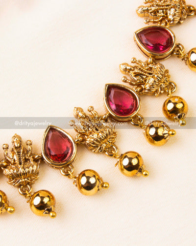 Zoomed-in view of ruby red temple necklace showing Lakshmi Devi motifs and gold danglers.