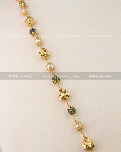 Detailed view of gold-finished chain with green enamel beads and pearl accents.