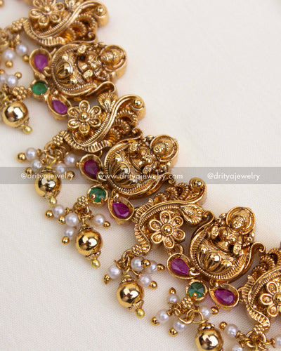 Detailed view of Lakshmi motifs and floral scrolls with pink and green stones and pearl-gold danglers.