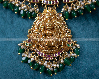 Close-up of the intricately detailed Lakshmi pendant from Dritya Jewelry's temple necklace set, showcasing green bead accents and traditional motifs.