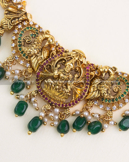 Close-up showing detailed peacock carvings, ruby-green stonework, and Lakshmi motif pendant with green bead drops.
