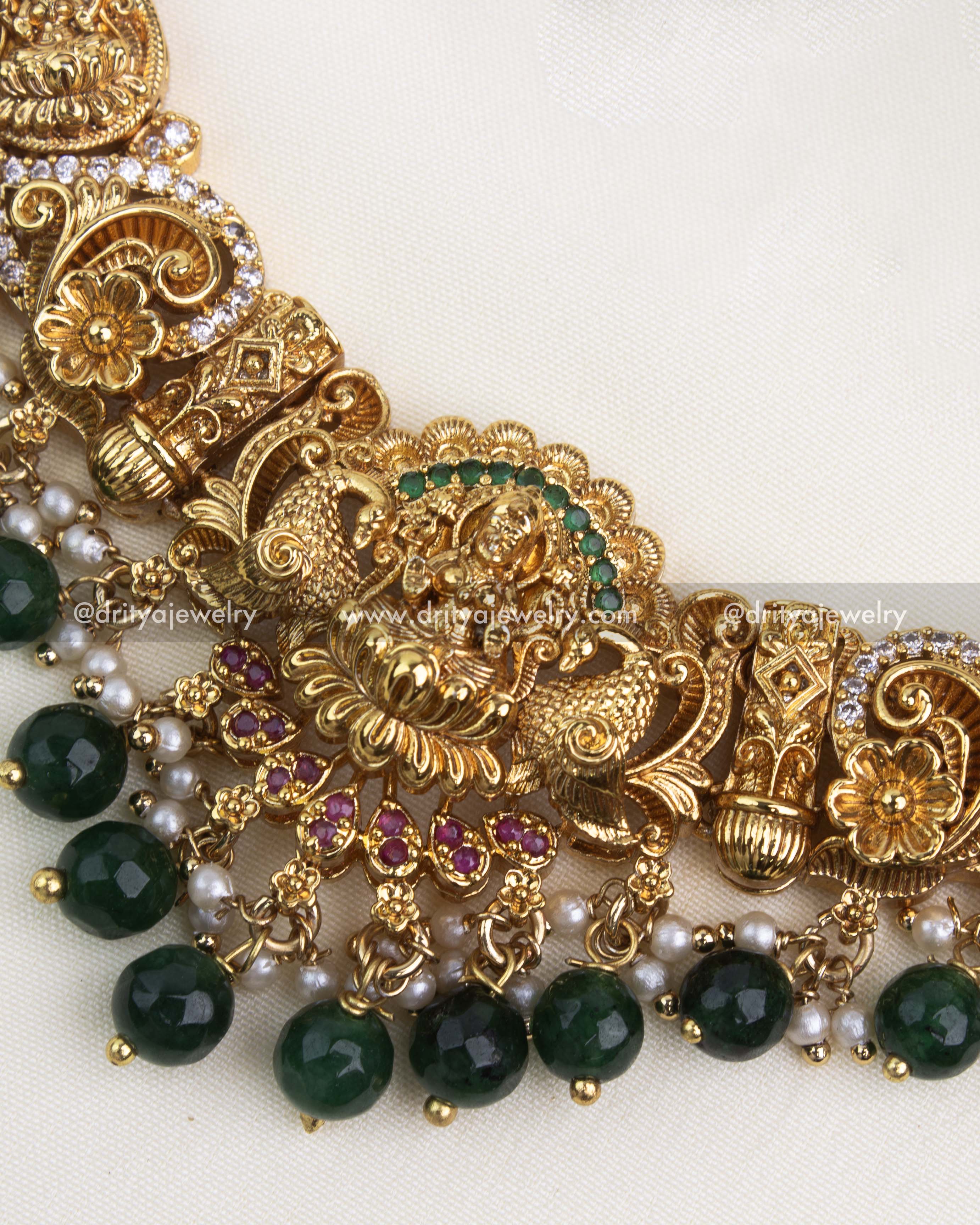 Detailed close-up of Nakshi pendant with ruby accents, green beads, and antique gold finish.