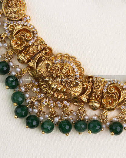 Detailed close-up of antique gold Nakshi pendant with white stones and green bead edging.