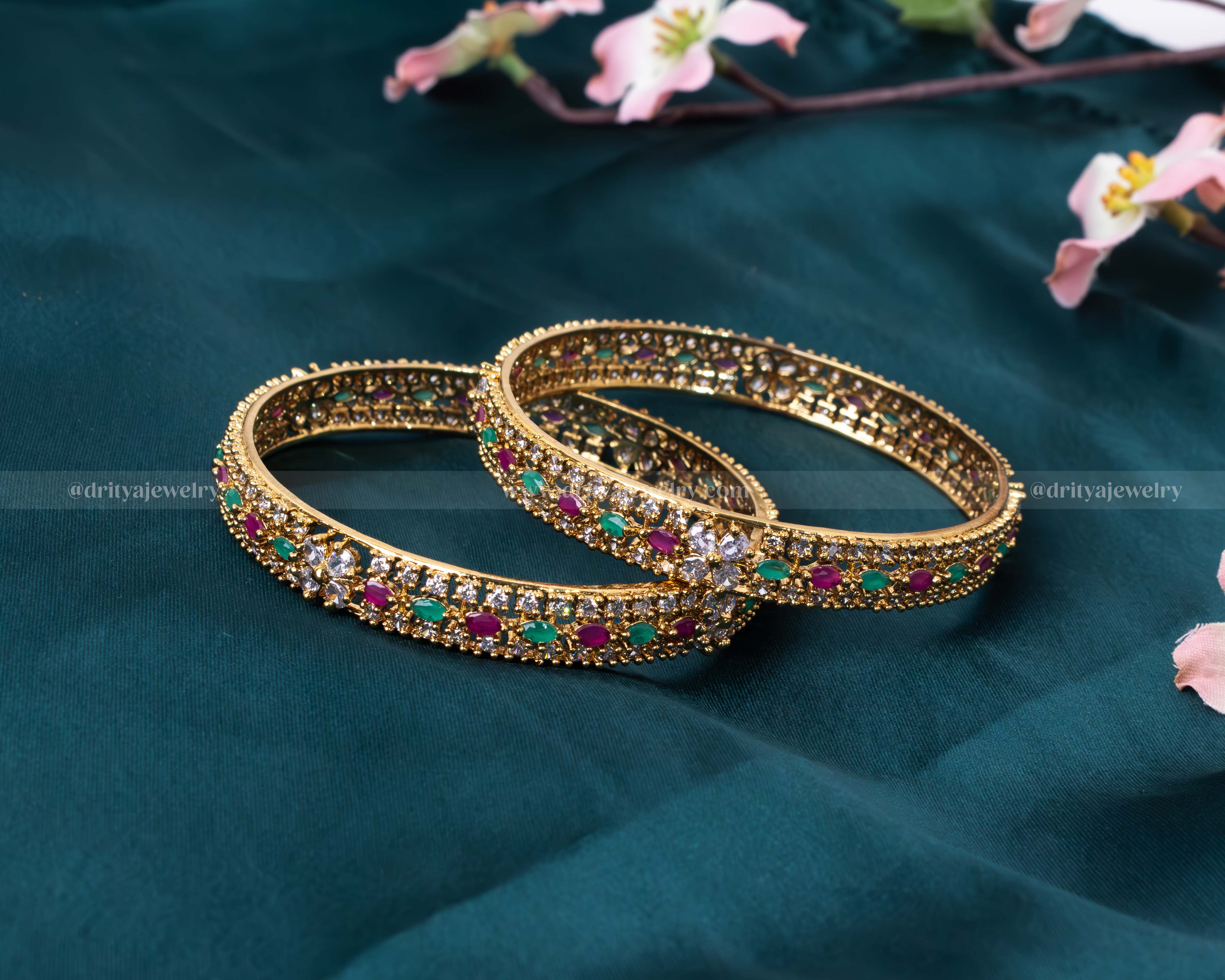 Elegant pair of gold bangles encrusted with emeralds, rubies, and diamonds from Dritya Jewelry.