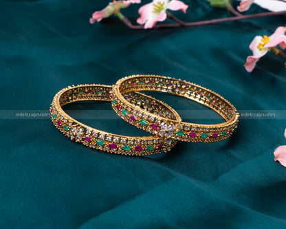 Elegant pair of gold bangles encrusted with emeralds, rubies, and diamonds from Dritya Jewelry.