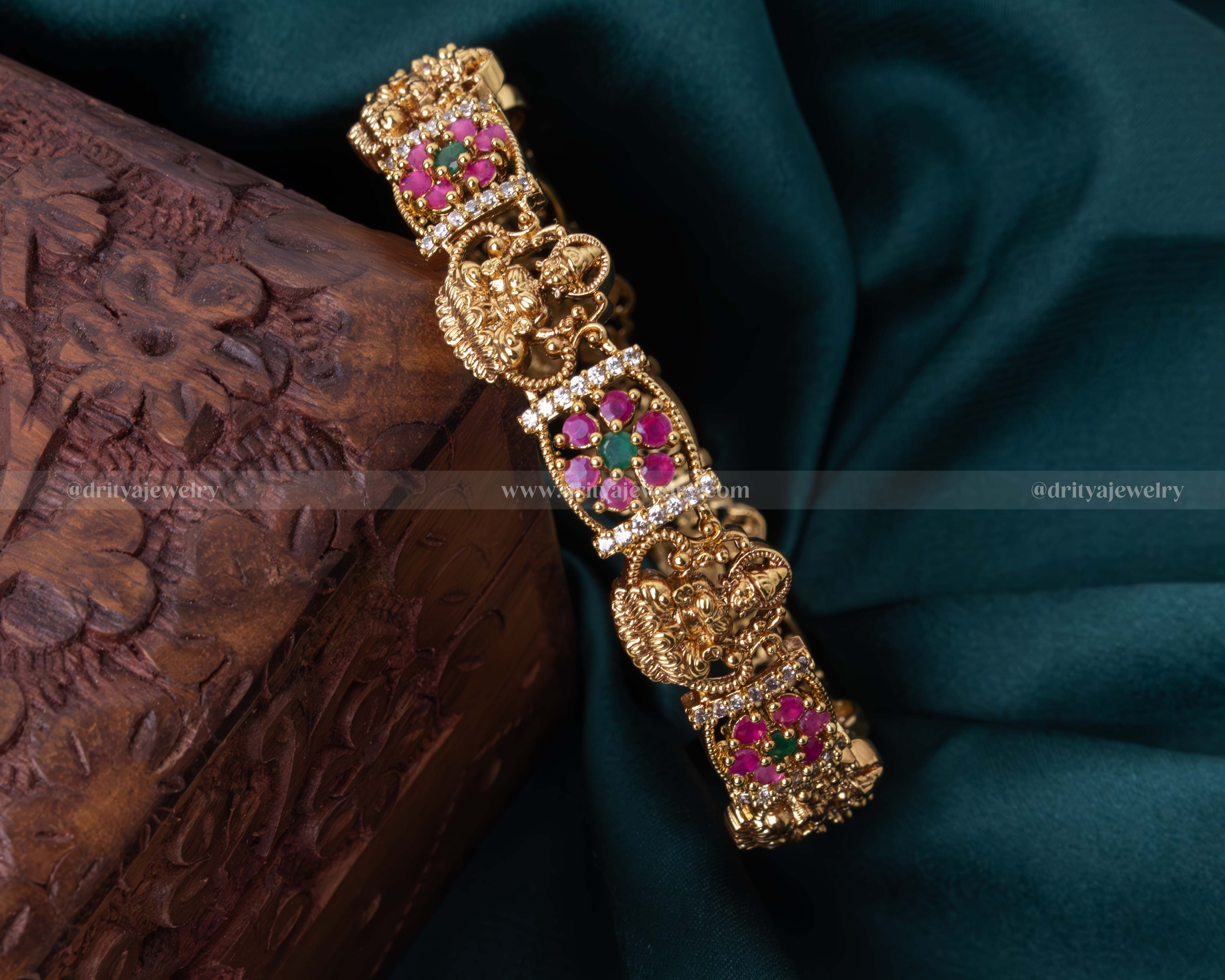 Gold-tone Temple bangle with Lakshmi Devi motif and pink gemstone embellishments, perfect for traditional celebrations.