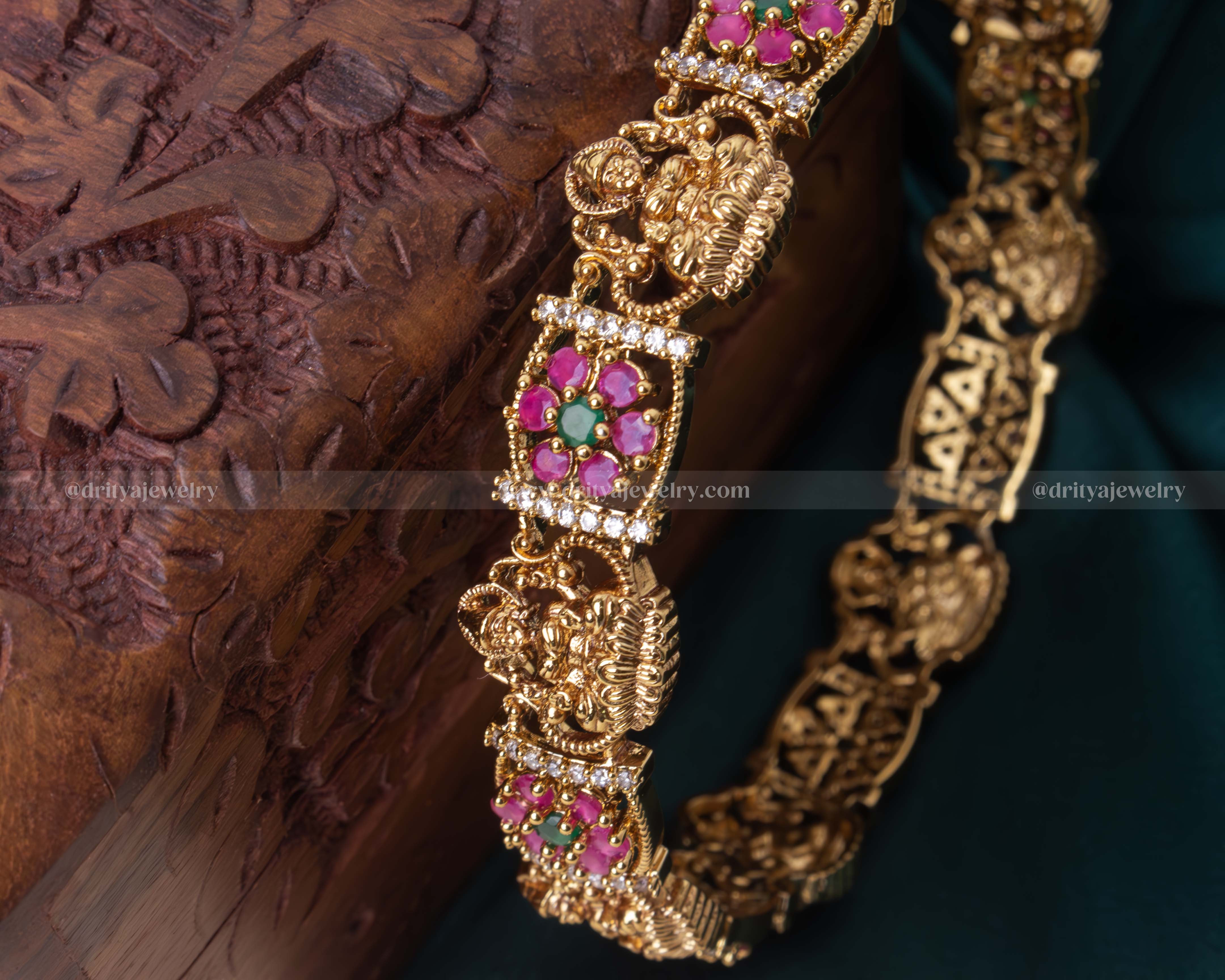 Gold-tone Temple bangle with Lakshmi Devi motif and pink gemstone embellishments, perfect for traditional celebrations.