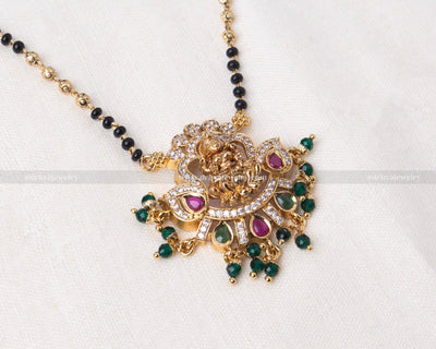 Elegant black beads necklace with a detailed gold Lakshmi Devi pendant adorned with green and pink gemstones, perfect for religious occasions and festive wear.
