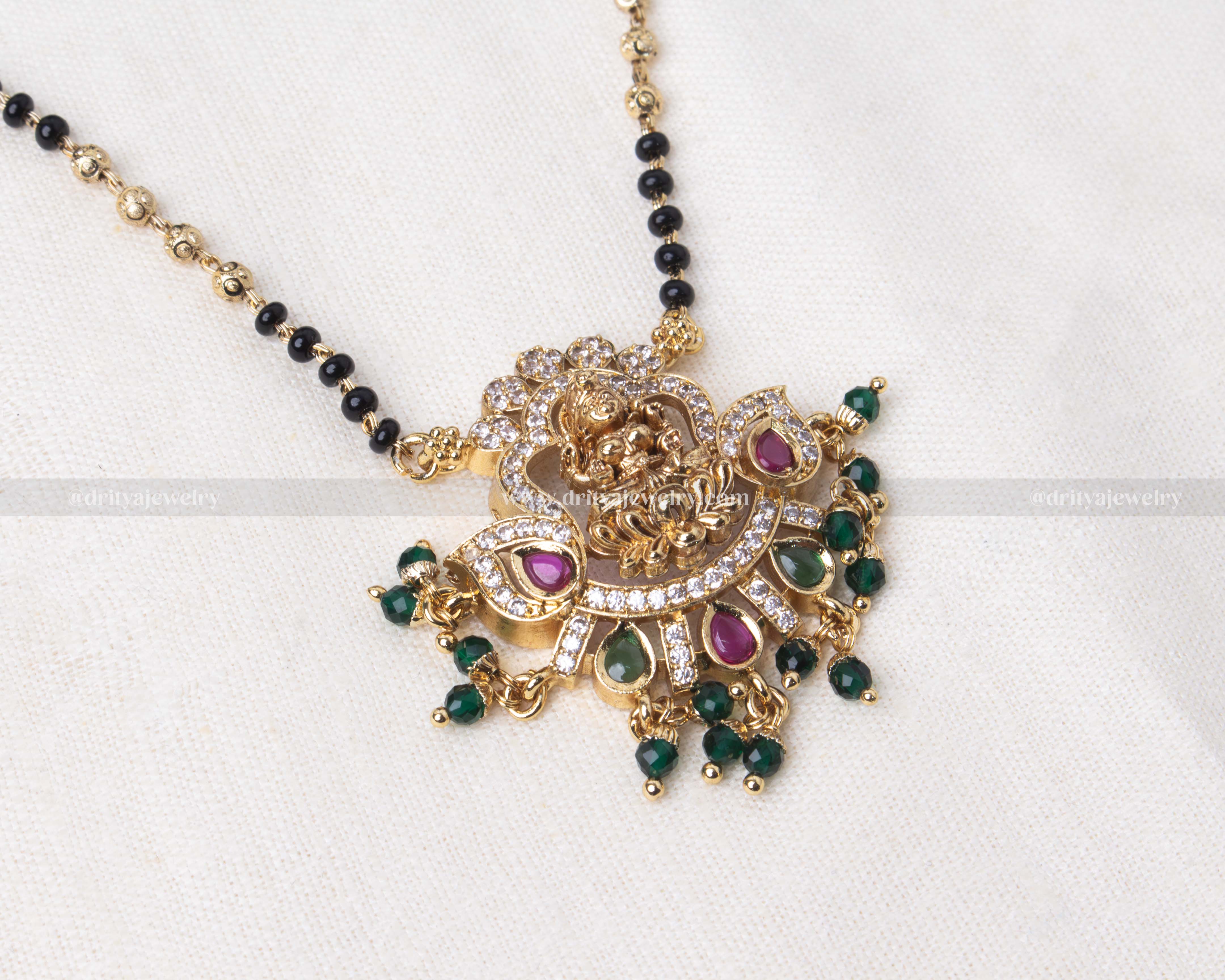 Elegant black beads necklace with a detailed gold Lakshmi Devi pendant adorned with green and pink gemstones, perfect for religious occasions and festive wear.