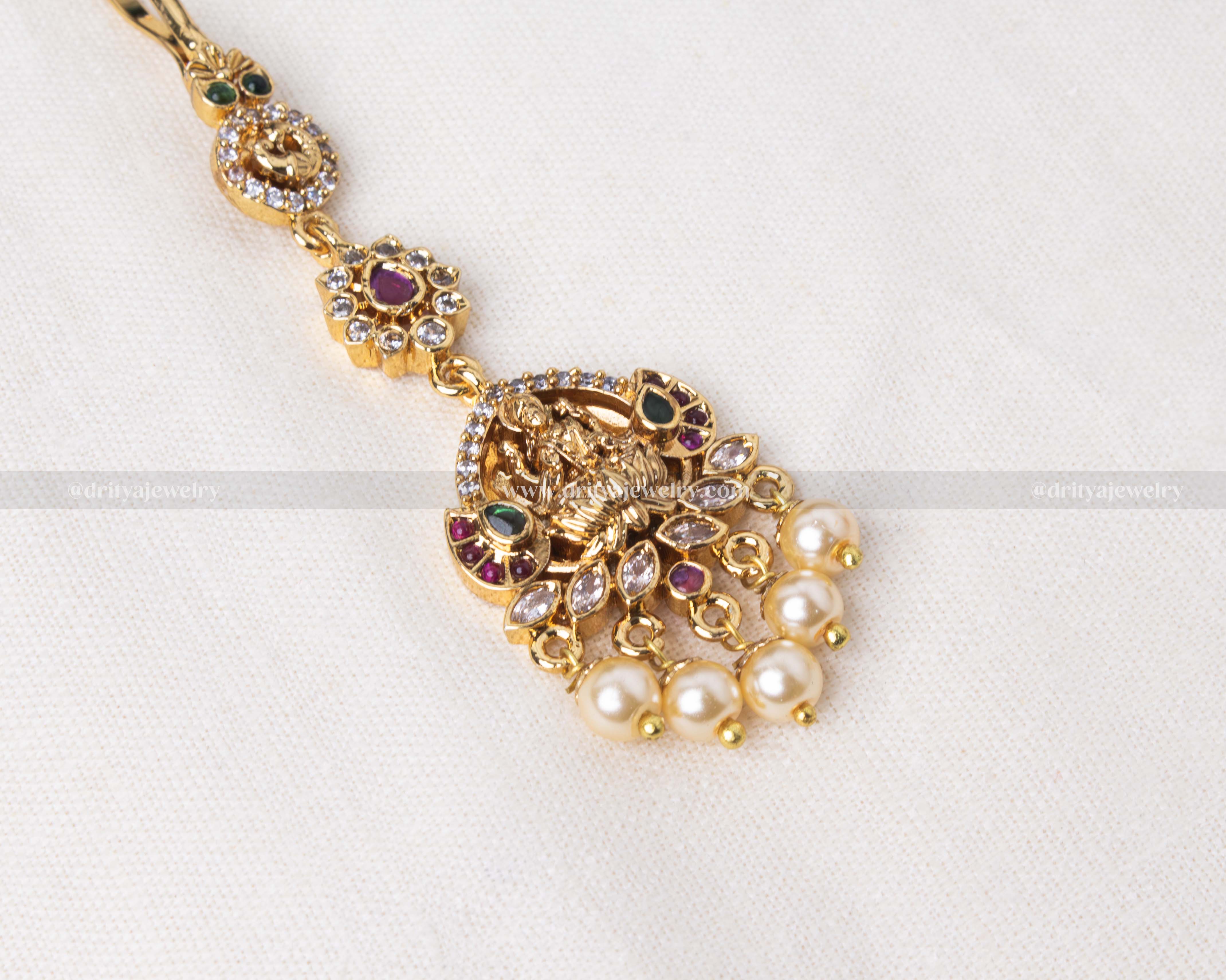 Gold polished Maang Tikka featuring a detailed Lakshmi Devi motif adorned with colorful gemstones and pearl accents, ideal for spiritual and traditional occasions.