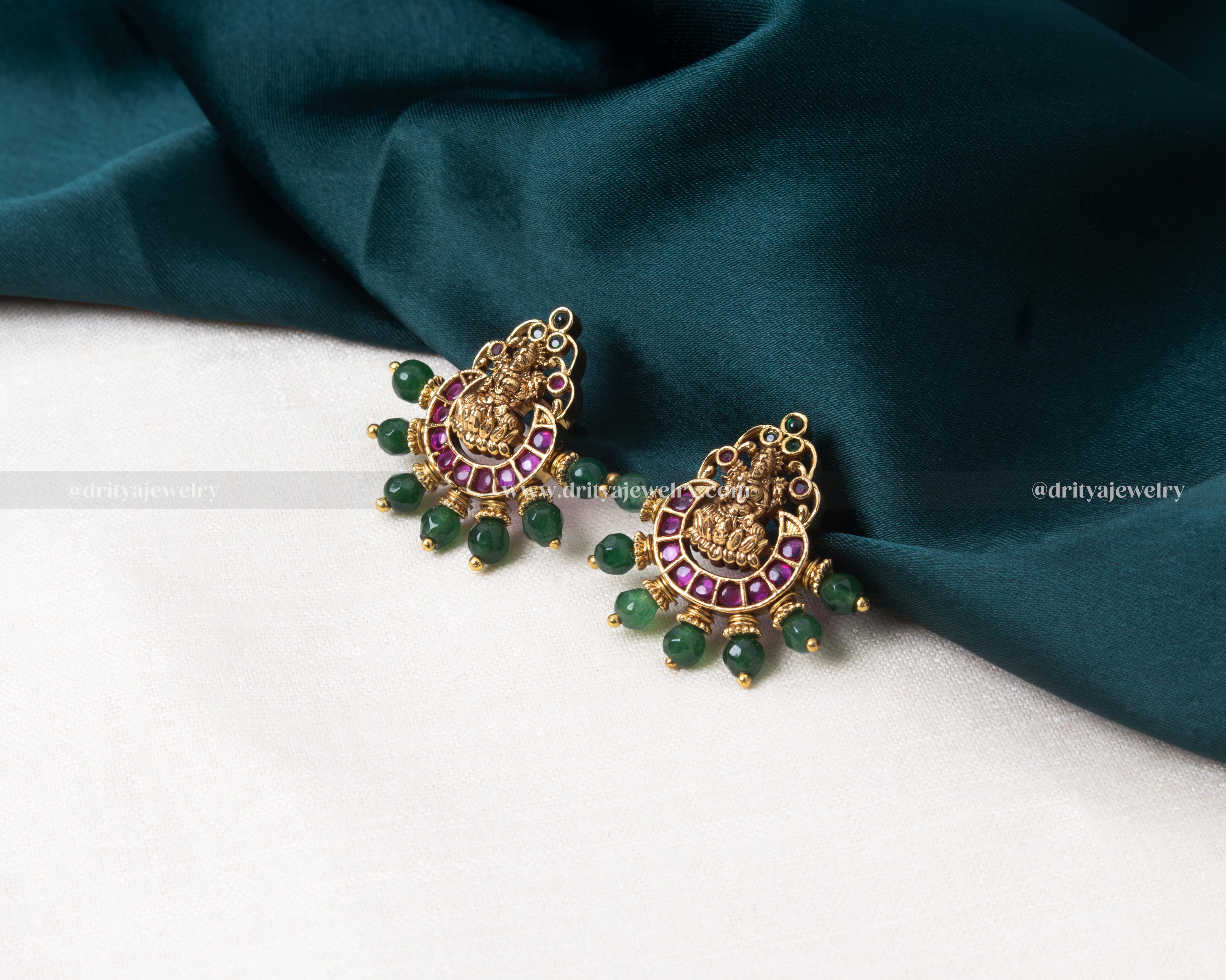 Elegant Lakshmi Devi motif stud earrings with emerald accents and pearl embellishments.