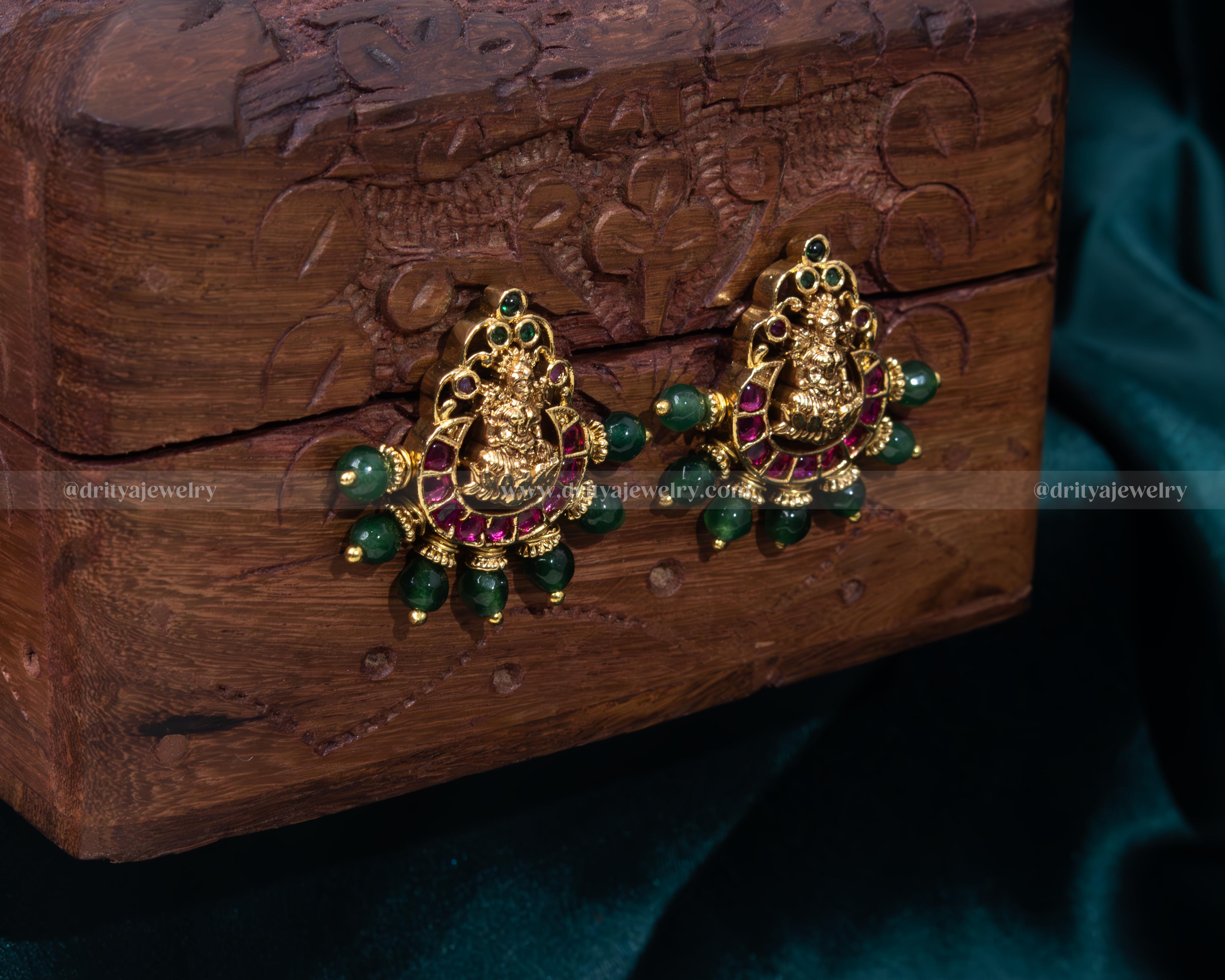 Elegant Lakshmi Devi motif stud earrings with emerald accents and pearl embellishments.