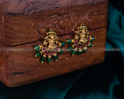 Elegant Lakshmi Devi motif stud earrings with emerald accents and pearl embellishments.