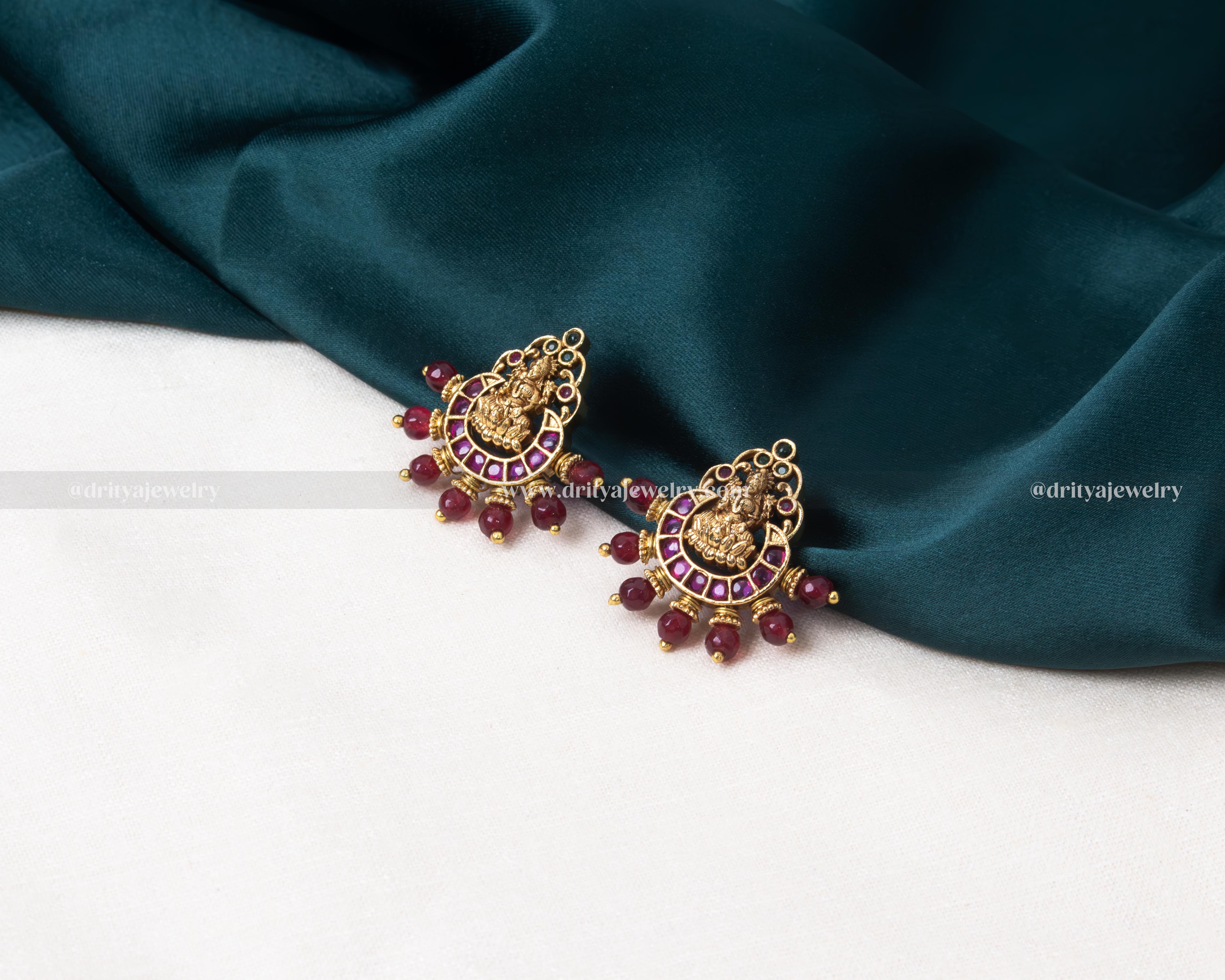 Exquisite Lakshmi Devi motif stud earrings with ruby beads and intricate golden settings.