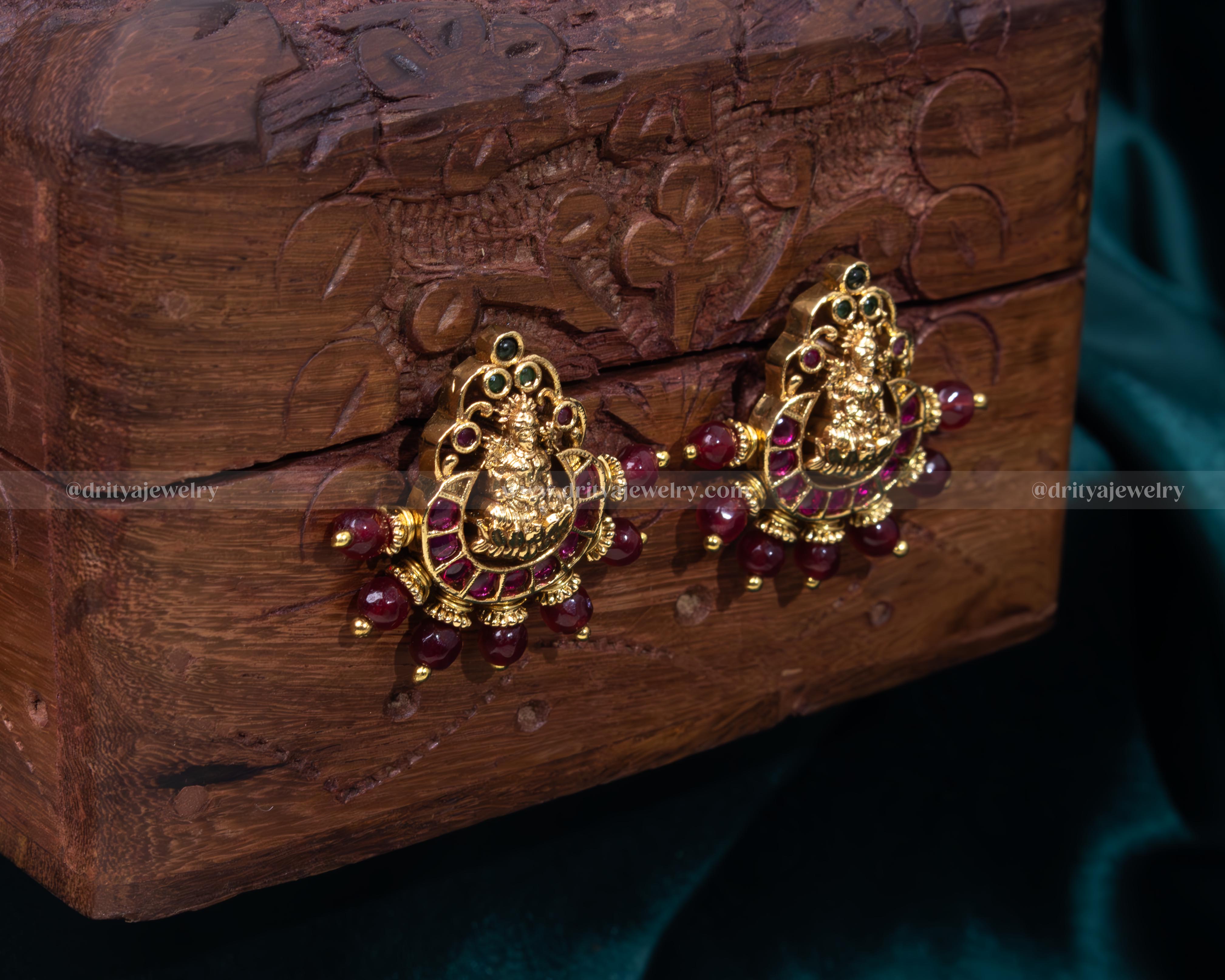 Exquisite Lakshmi Devi motif stud earrings with ruby beads and intricate golden settings.