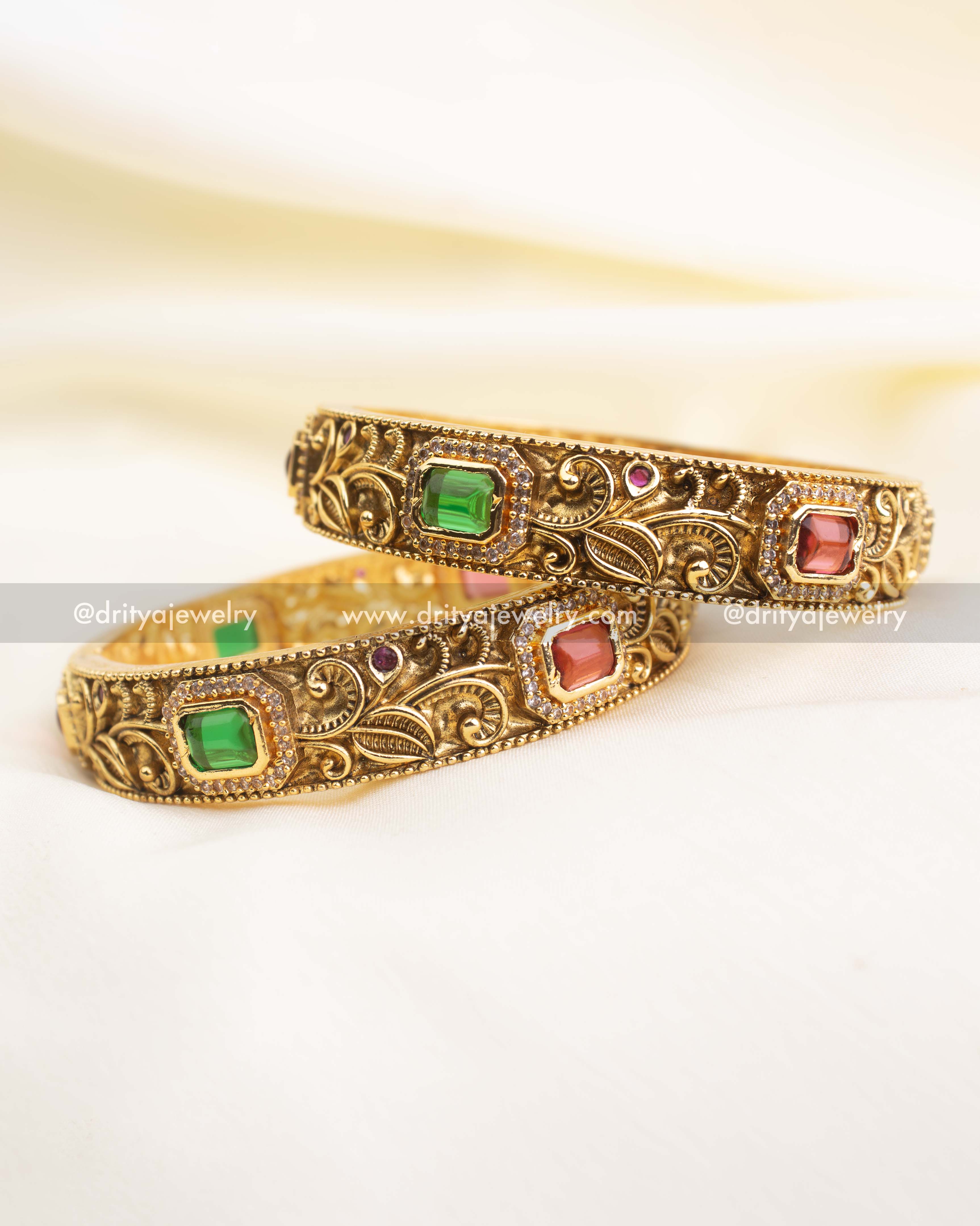 Intricately carved antique bangles featuring alternating ruby and emerald stones bordered with CZ detailing.