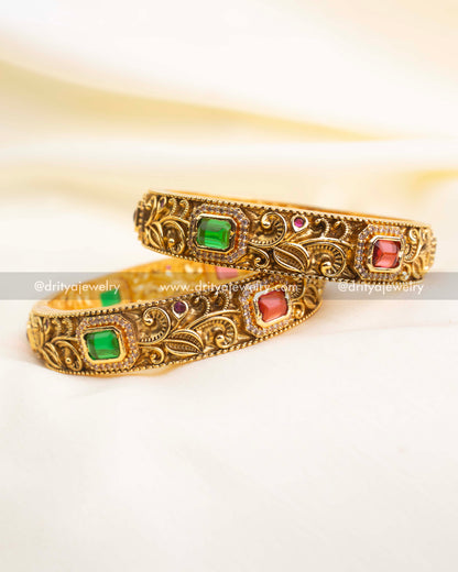 Intricately carved antique bangles featuring alternating ruby and emerald stones bordered with CZ detailing.