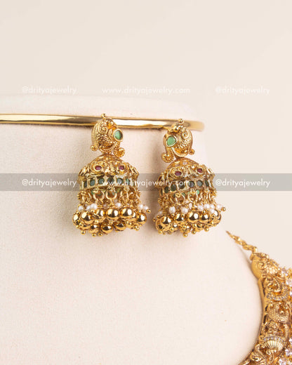 Gold jhumkas with ruby-green stones, parrot motifs, and pearl bead detailing.