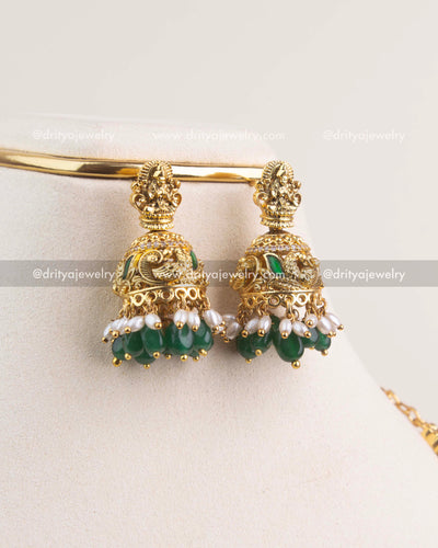 Gold jhumka earrings with Lakshmi motif, green beads, and pearl detailing.
