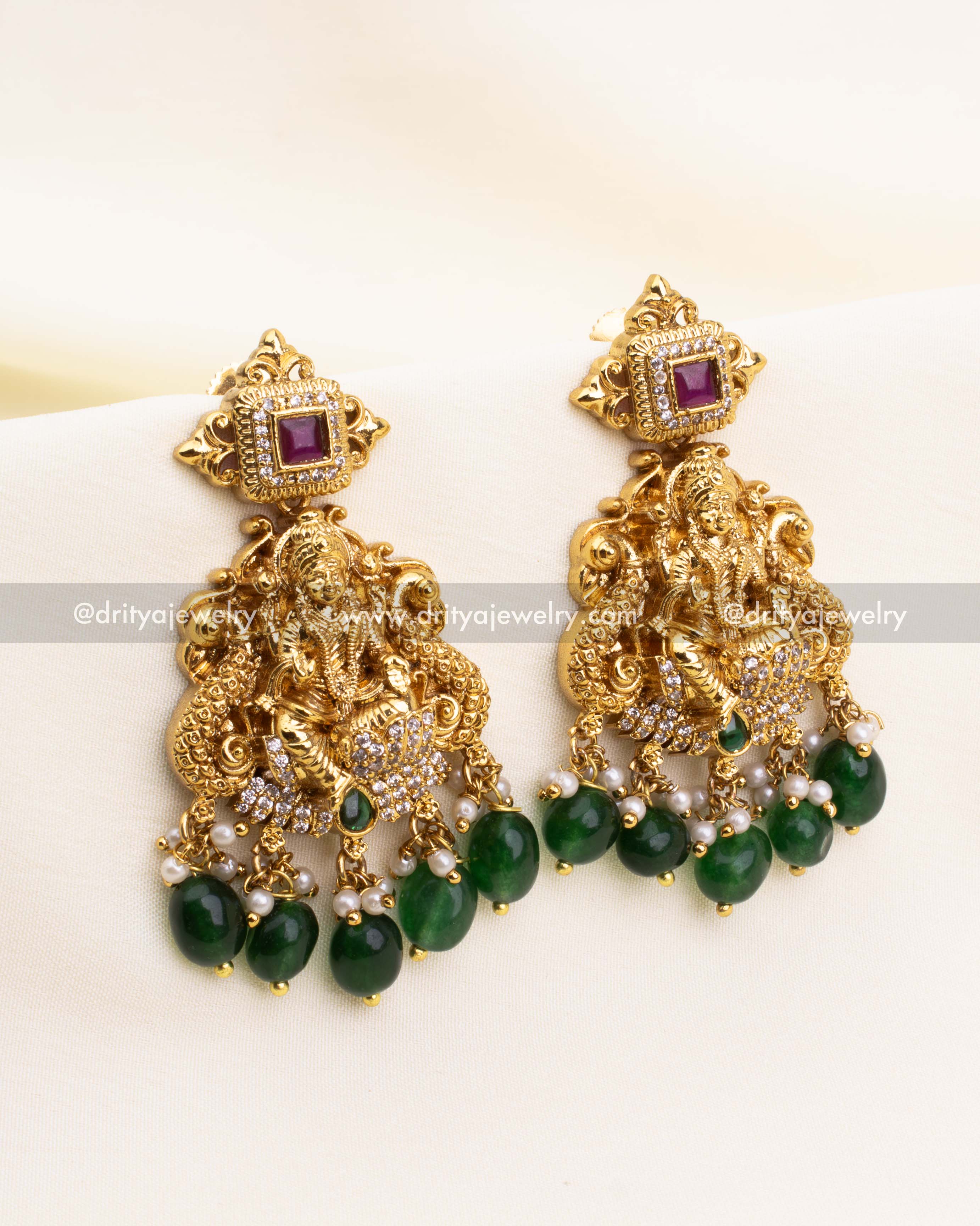 Temple-style earrings with Lakshmi Devi idol, ruby studs, and pearl-green bead hangings.