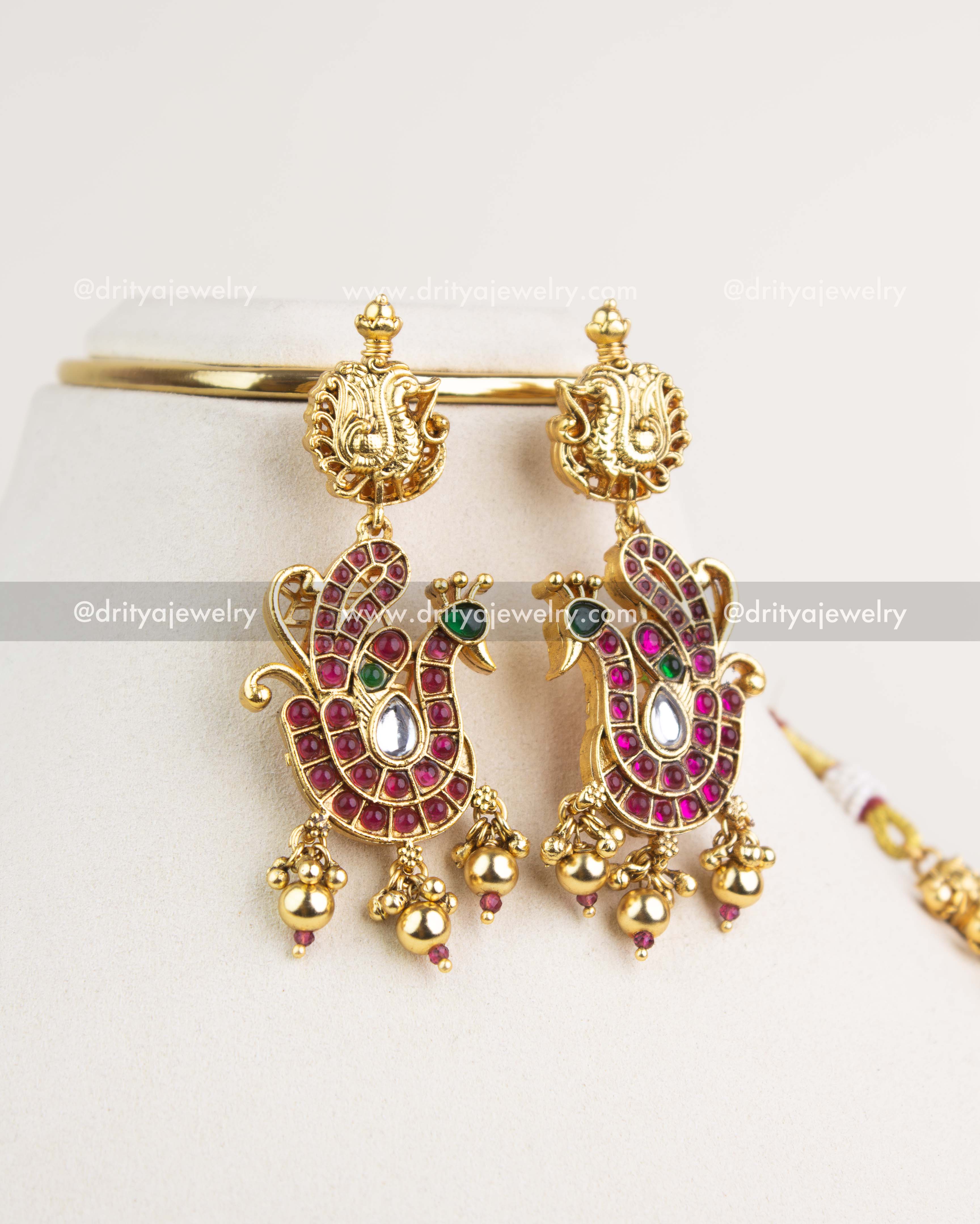 Peacock-inspired earrings with ruby stones, kundan work, and gold bead hangings in antique finish.