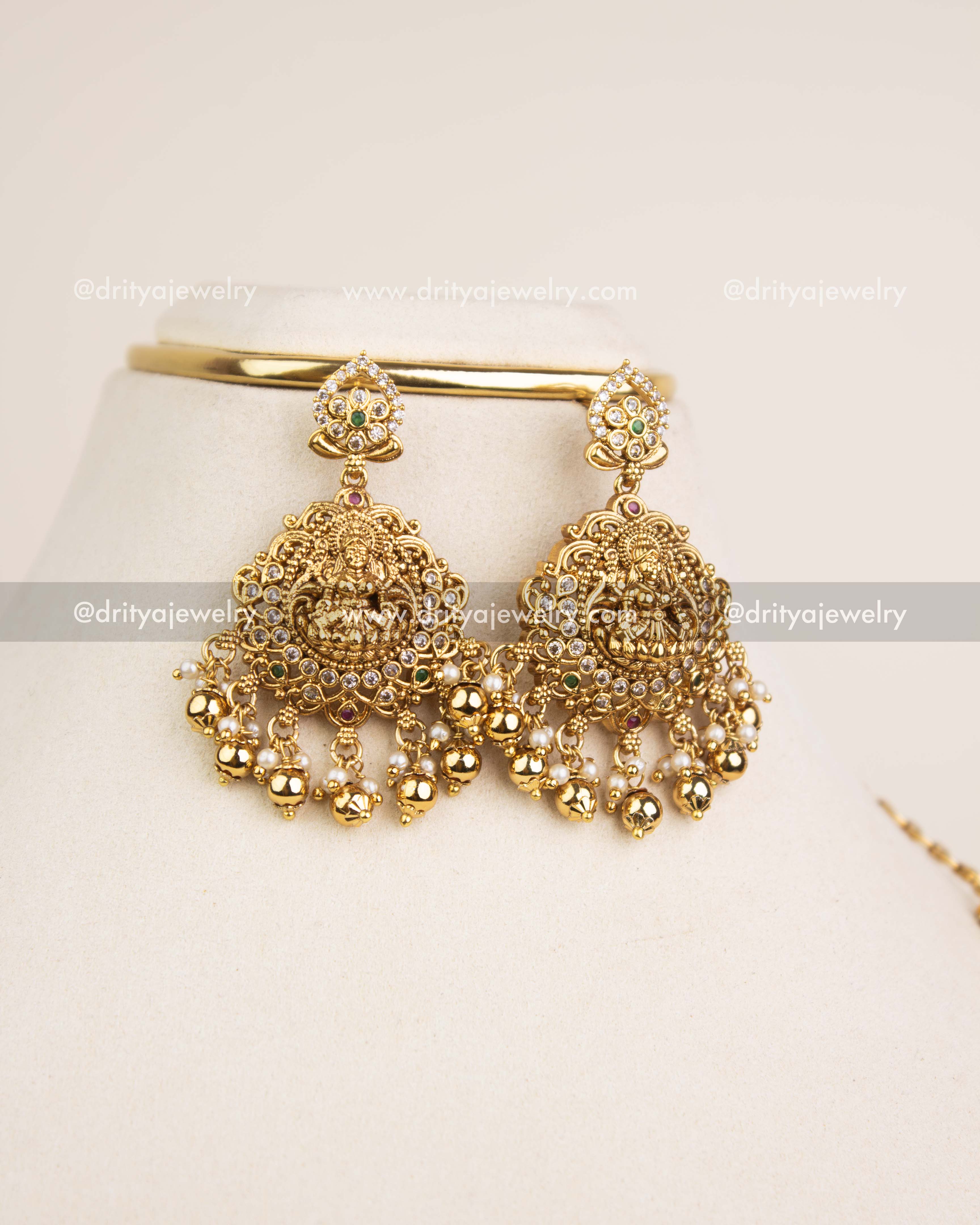 Gold polish temple-style jhumka earrings with Lakshmi motif and bead hangings.