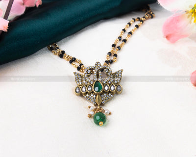 Luxurious black beads necklace featuring a gold-plated lotus-inspired pendant with green and red gemstone embellishments, blending tradition with modern elegance.