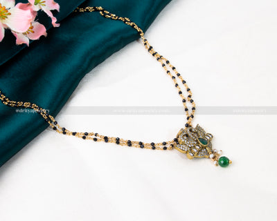 Luxurious black beads necklace featuring a gold-plated lotus-inspired pendant with green and red gemstone embellishments, blending tradition with modern elegance.