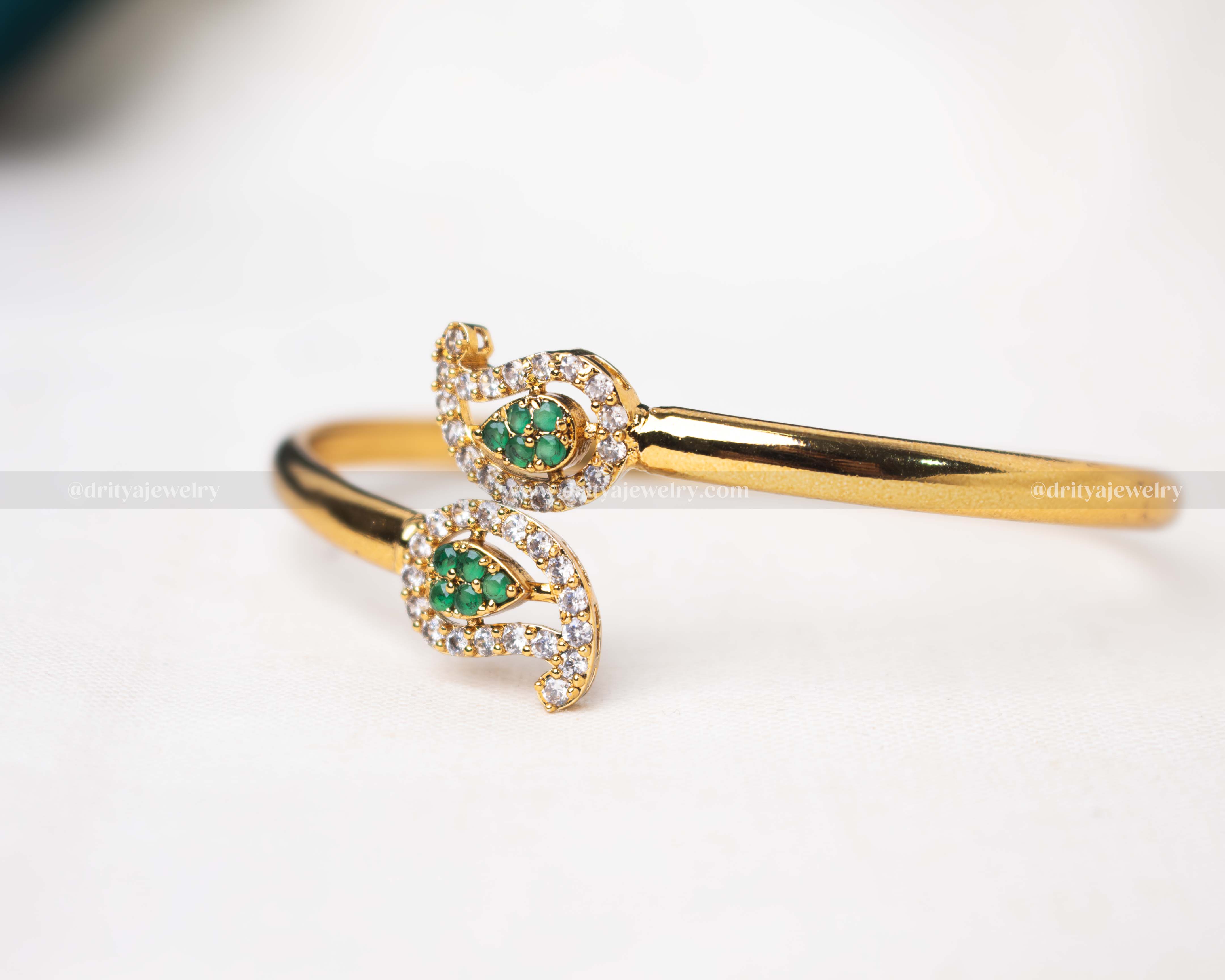 Flexible gold kadas adorned with vibrant pink and green stones, showcasing an elegant swirl design with sparkling accents.