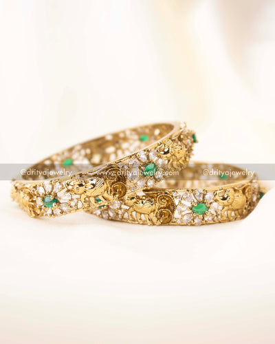 Close-up of gold-plated bangles featuring elephant designs and green CZ stones.