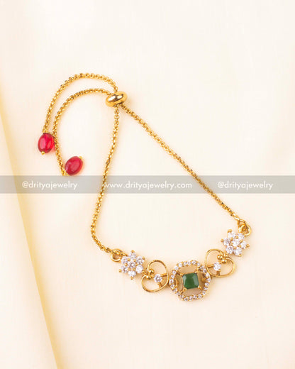 Square-cut emerald green stone surrounded by CZ detailing in a floral gold motif.